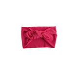 A bright pink textured fabric headband with a large twisted knot in the center, displayed flat against a solid white background.