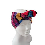 A multicolor patterned fabric headwrap with a large bow, displayed on a white mannequin head against a plain white background.