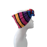 A multicolor striped headwrap turban hat with a knotted top, displayed on a white mannequin head in profile against a white background.