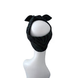 A black fabric headband with a subtle dark green tiger stripe pattern, styled on a white mannequin head with a bow at the top, set against a plain white background.