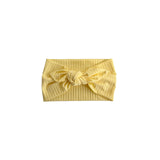 A pale yellow ribbed fabric headband with a large bow at the center front, displayed flat against a solid white background.