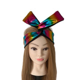 A mannequin head with long light brown hair wearing a large shiny rainbow bow headband with black trim, shown against a plain white background.