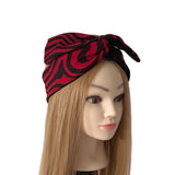 A red and black patterned fabric headwrap or hair tie styled on a mannequin head with long blonde hair against a plain white background.