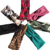 Six twisted fabric headbands arranged in a circle on a white background, showing different patterns and colors: leopard print, black, teal, camouflage, red plaid, and solid pink.
