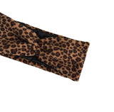 A close-up of a leopard print headband with a twisted knot detail, featuring a brown and black animal pattern on a white background.
