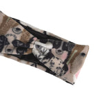 A close-up of a plush knit headband with a twisted knot design, featuring a multicolor animal print pattern in brown, black, white, and pink on a white background.