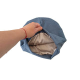 Hand holding a blue fabric beanie with beige interior on a white background