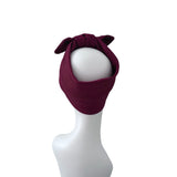 A dark burgundy ribbed knit headband with a large bow on top, displayed on a white mannequin head against a plain white background.