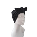 A black fabric headwrap turban hat with a large bow on top, displayed on a white mannequin head against a plain white background.