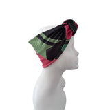 A multicolor patterned headband with black, green, and pink sections, knotted on a white mannequin head in profile against a white background.