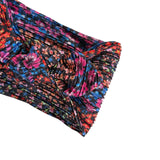 A close-up of a pleated fabric accessory, likely a headband or hair wrap, featuring a vibrant multicolor floral pattern on a black background.
