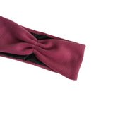 A close-up of a twisted fabric headband in a deep berry pink color, showing a black inner lining, set against a plain white background.