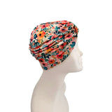 A multicolor floral turban hat displayed on a white mannequin head in profile against a solid white background.
