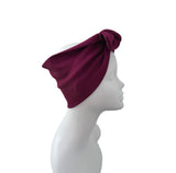 A deep burgundy ribbed fabric headwrap or turban hat styled on a white mannequin head in profile against a solid white background.