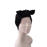 A black fabric headwrap turban hat with a large bow on top, displayed on a light gray mannequin head against a plain white background.