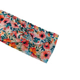 A fabric headband with a large twisted knot, featuring a vibrant watercolor floral pattern with pink, orange, and teal flowers on a light cream background.