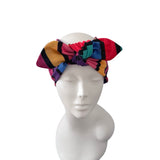 A multicolor patterned headwrap headband with a large bow, displayed on a white mannequin head against a plain white background.