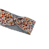 A fabric headband with a twisted knot, featuring a multicolor autumn leaf pattern on a cream background with a solid heather gray reverse side.