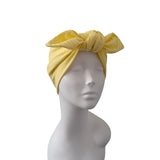 A yellow crinkle-textured fabric headwrap turban hat styled on a white mannequin head, shown against a plain white background.