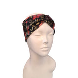 A black twisted headband with a red and green floral butterfly pattern, displayed on a white mannequin head against a white background.