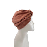 A ribbed knit twisted turban-style headband in a muted terracotta brown color, displayed on a white mannequin head in profile against a plain white background.