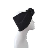 A black fabric headwrap or turban-style headband shown on a white mannequin head in side profile against a plain white background.