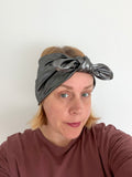 A woman wearing a metallic dark gray knotted headband and a brownish-red long-sleeve shirt, photographed against a plain light background.