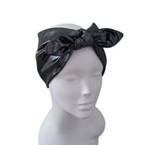 A black satin-like headwrap or turban-style headband with a large bow, displayed on a white mannequin head against a plain white background.
