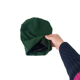 Green knit beanie held by a hand against a white background