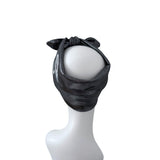 A black metallic headband with a knotted bow design at the top, displayed on a white mannequin head against a plain white background.