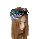 A multicolor patterned silk headband with a bow, styled on a mannequin head with long light brown hair against a white background.