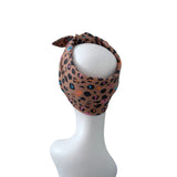 A leopard print headband with a tie-front knot, displayed on a white mannequin head against a solid white background.