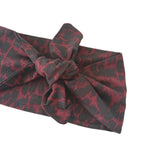 Red and black patterned headband with a bow on a white background
