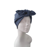 A navy blue fabric headwrap or turban hat with a large bow detail on top, displayed on a white mannequin head against a plain white background.