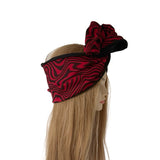 A red and black wavy patterned headband with a large matching bow, displayed on a blonde mannequin head against a white background.