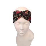 A black twisted headband with a red, pink, and green floral butterfly pattern, displayed on a white mannequin head against a white background.