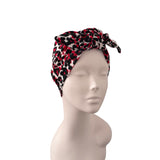 A knotted headwrap or turban hat with a red, black, and white abstract pattern, displayed on a light gray mannequin head against a plain white background.