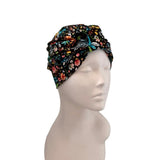A multicolor floral and butterfly patterned fabric headwrap turban cap displayed on a light gray mannequin head against a white background.