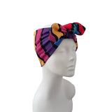 A multicolor striped and wavy patterned headwrap turban hat displayed on a white mannequin head against a solid white background.