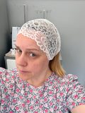 Person wearing a white lace head covering in a sewing room.