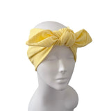 A yellow crinkle-textured fabric headwrap with a large twisted bow, displayed on a white mannequin head against a plain white background.