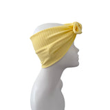 A light yellow ribbed fabric headband with a twisted knot and matching fabric flower accent, displayed on a white mannequin head in profile against a plain white background.