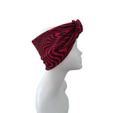 A red and black wavy patterned headband displayed on a white mannequin head in profile against a plain white background.